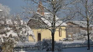 Paisaje nevado con un edificio amarillo que destaca por una torre prominente, rodeado de árboles cubiertos de nieve y una cerca.