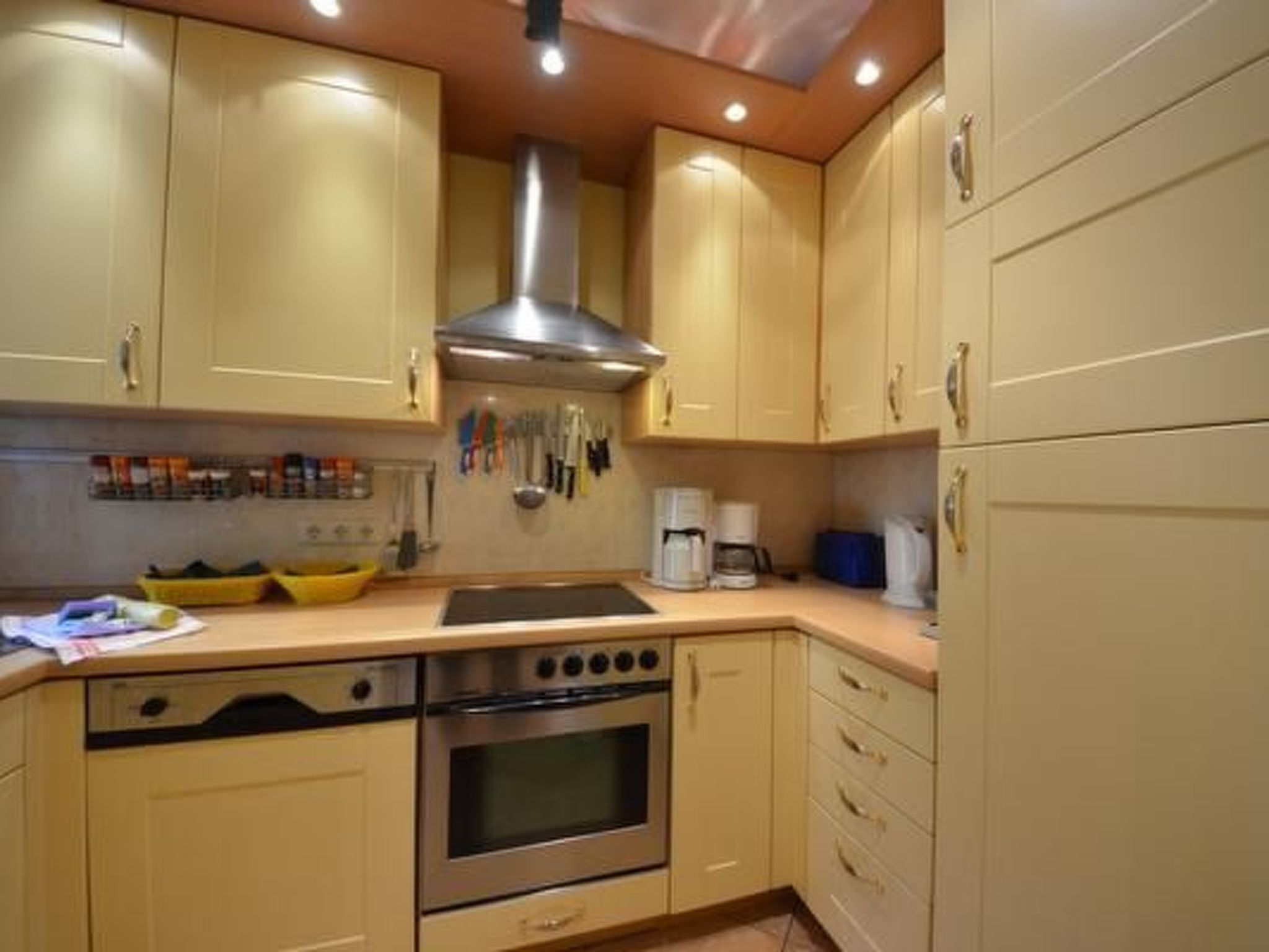 A kitchen with beige cabinets, a stainless steel range hood, a stove, and a coffee maker.
