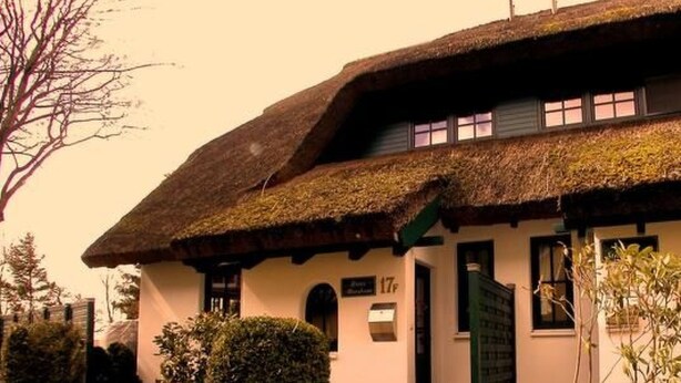 Une maison traditionnelle avec un toit de chaume, un petit porche et une plaque portant le numéro « 17 ».