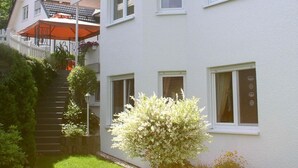 A two-story house with a white exterior, multiple windows, and a small garden with a tree. - Apartment Wiese by Interhome (Bruchhausen)