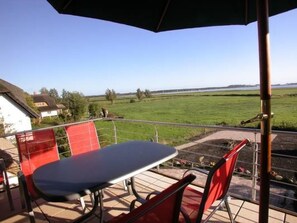 An outdoor patio with a table and chairs, a view of a green field, and a building in the background. - Sonnenkamp Maisonette by Interhome (Baabe)
