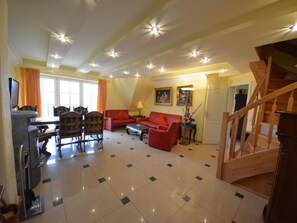 Un salon spacieux comprenant un coin repas, un canapé rouge et un escalier en bois.