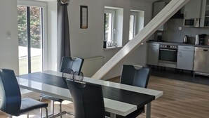 Eine moderne Küche mit Edelstahlgeräten, ein Essbereich mit Glastisch und schwarzen Stühlen sowie eine Treppe, die in eine obere Ebene führt.
