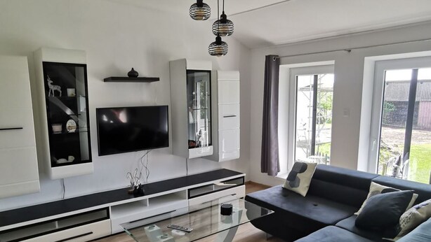 Ein modernes Wohnzimmer mit großem Flachbildfernseher, einem dunkelgrauen Sofa und einem Glastisch.