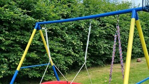 Een schommel met een rode zitting en een frame in geel en blauw.