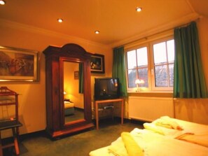 Habitación de hotel con cama, televisión, espejo y ventana con cortinas.