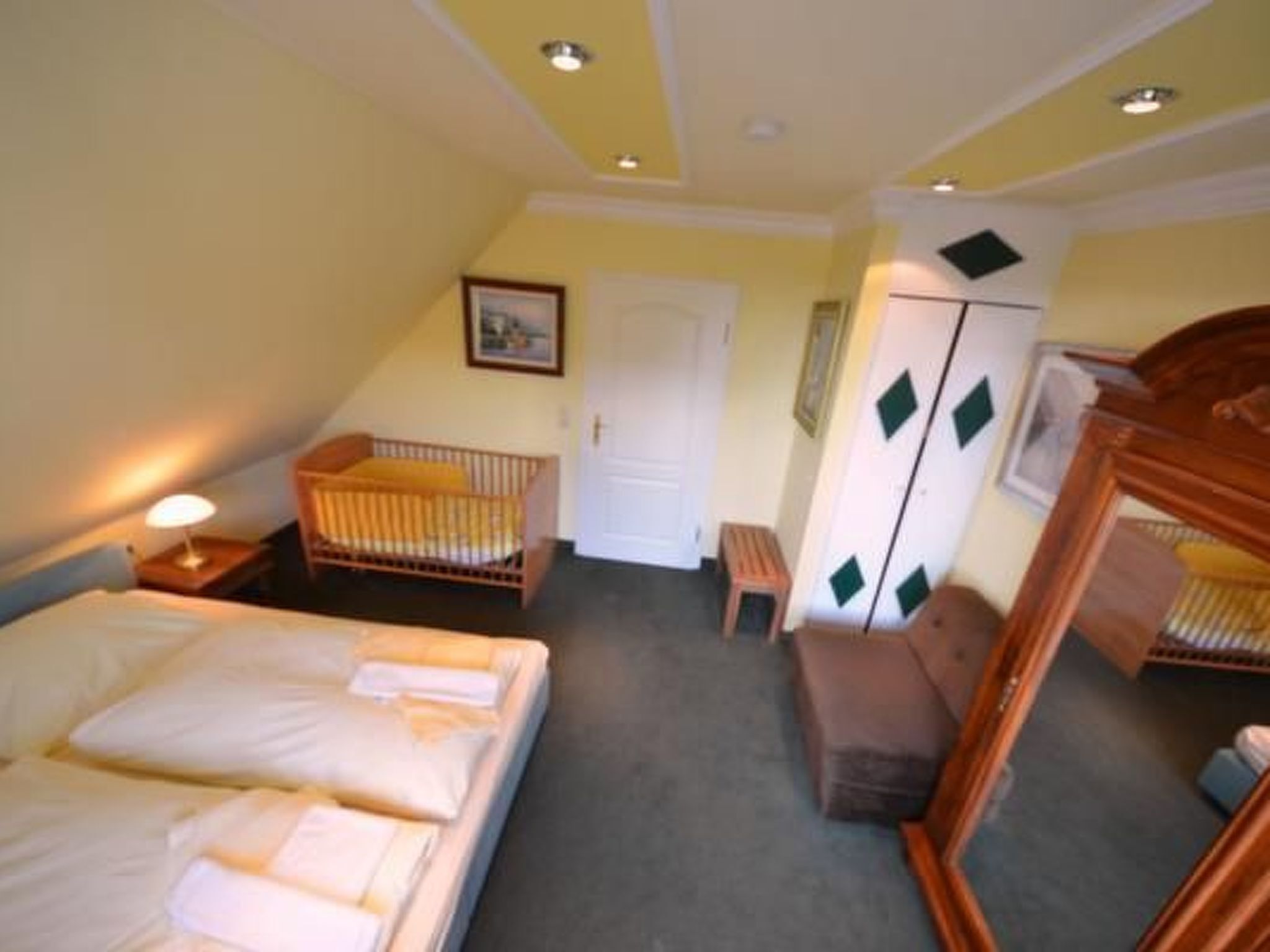 Een slaapkamer met een bed, een babybedje, een stoel, een garderobe en een spiegel.