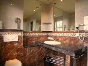 Un baño con tocador de mármol, un espejo grande y un secador de pelo en la pared.