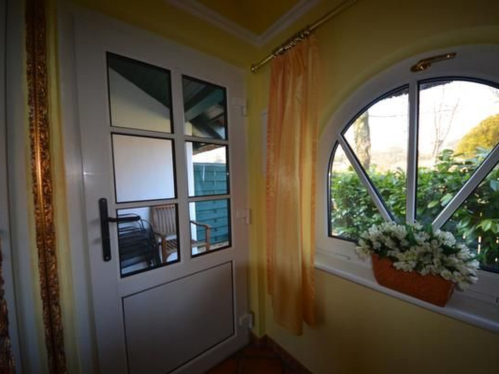 A room with a white door, a window with a view of greenery, and a curtain.