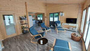 Une pièce spacieuse aux murs et au plancher en bois, comprenant un coin repas, un téléviseur et des sièges.