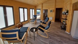 Une cabane en bois spacieuse, dotée d’un espace de vie comprenant plusieurs options d’assises, de grandes fenêtres et une table centrale.
