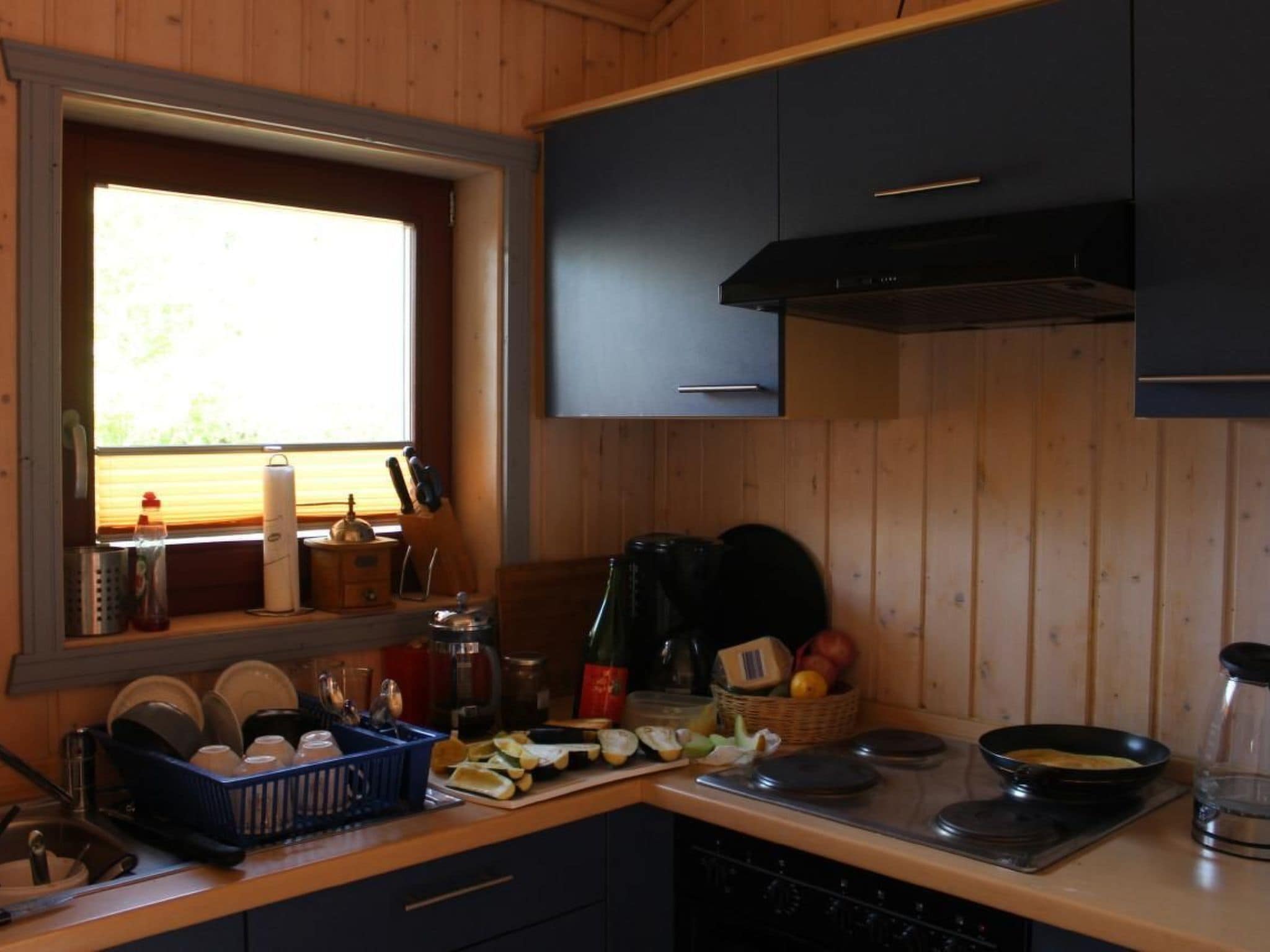 Eine Küche mit Holzausstattung, einem Fenster mit Jalousien, einer Spüle und verschiedenen Küchengegenständen auf der Arbeitsfläche.
