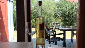 A bottle of wine and two glasses on a table with a view of a garden and outdoor seating area. - Pinto Béla by Interhome (Twist)