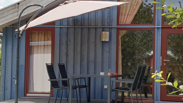 A modern outdoor patio with a table and chairs, a large umbrella, and a glass door leading to the interior. - Pinto Béla by Interhome (Twist)