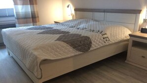 A neatly made bed with a quilted cover, a bedside table with a lamp, and a window with curtains.