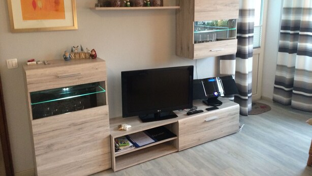 A modern living room with a flat-screen TV, wooden entertainment unit, and decorative items.