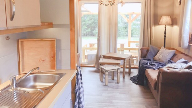 Ein gemütliches Blockhäuschen mit Küchenzeile, Essbereich und Wohnzimmer mit Sofa und Lampe.