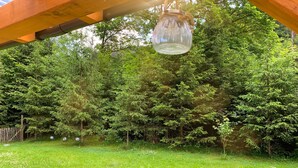 Ein Garten mit einer Holzw pergola, einem hängenden Glasbehälter und einem dichten Wald im Hintergrund.