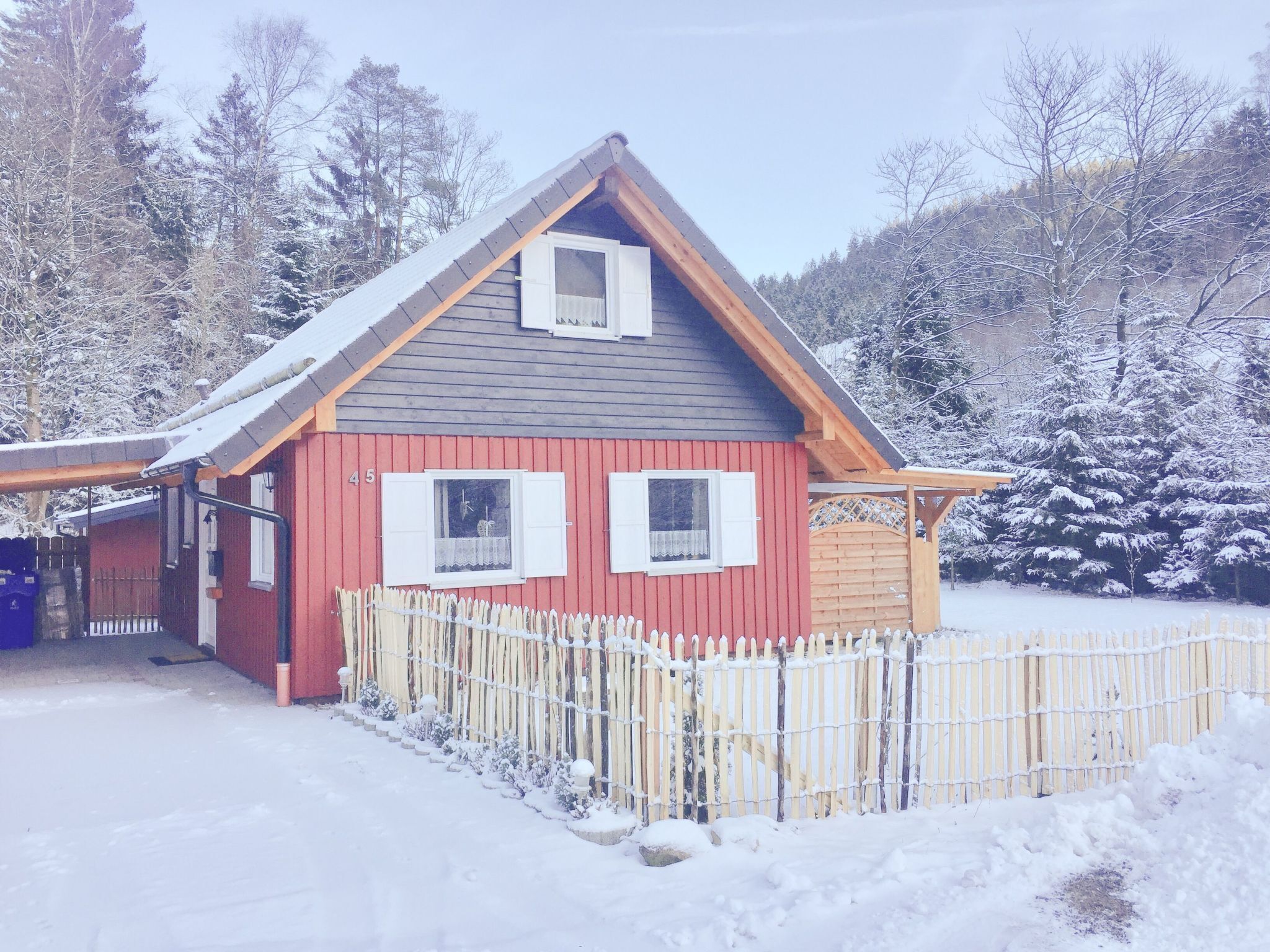 Ein rotes Holzhaus mit geneigtem Dach, weißen Fensterläden und einem Holzzaun.