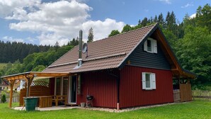 Eine rote Holzhütte mit geneigtem Dach, einem Schornstein und einer kleinen Veranda mit einer Bank.