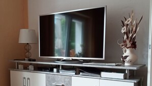 Un salon moderne avec un téléviseur à écran plat posé sur un meuble, une lampe et un vase décoratif.