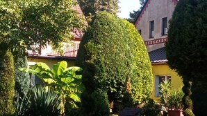 Une cour avec le clocher d’une église, des haies soigneusement taillées et un bâtiment jaune.