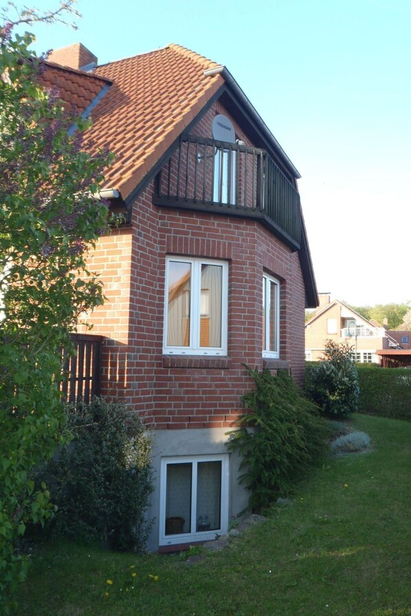 Et toetagers hus med facade af mursten, en balkon og en lille forhave med græsplæne og buske.