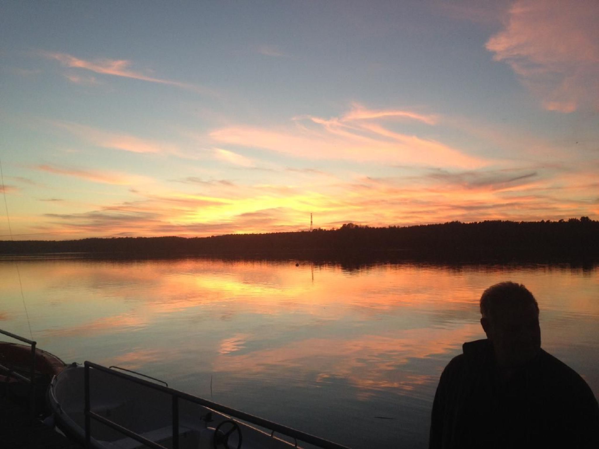 Iemand in een boot met uitzicht op een zonsondergang boven een rustig meer.