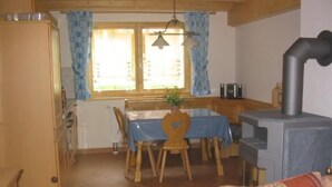 A cozy dining area with a wooden table and chairs, a stove, and a window with curtains. - Chalet Sachrang by Interhome (Aschau im Chiemgau)