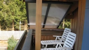 A covered outdoor area with two white lounge chairs and a table, surrounded by wooden beams and a metal railing. - Chalet Sachrang by Interhome (Aschau im Chiemgau)