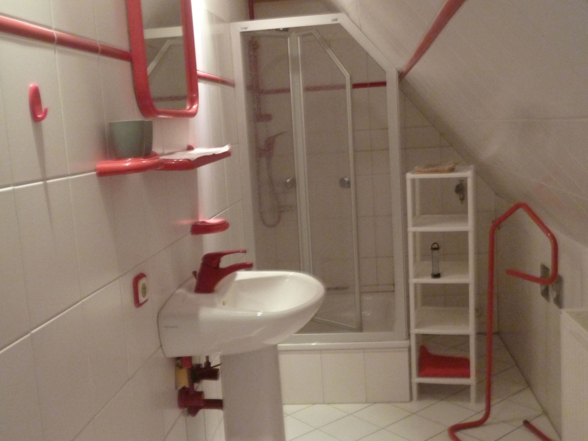 A bathroom with a white sink, red fixtures, a glass shower enclosure, and a white tiled floor.
