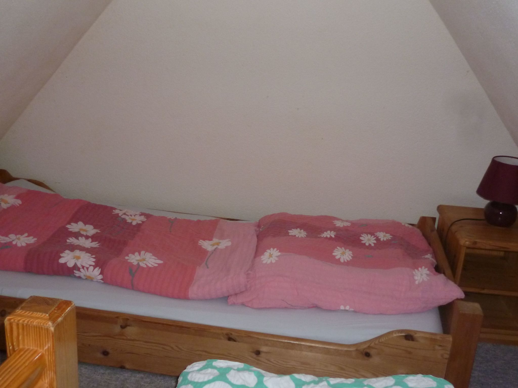 Ein Einzelbett mit rosa Blumendekoration und zwei Kissen, ein Nachttisch aus Holz mit einer Lampe sowie ein Holz-Kopfteil.