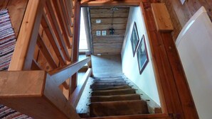Eine Holztreppe mit Handlauf, die zu einem Raum mit Holzwänden und einer Decke mit freiliegenden Balken führt.