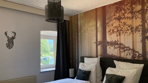 Ein Schlafzimmer mit zwei Betten, einer Hirschgeweih-Wanddekoration, einer Wand mit Waldmotiv und einem Fenster mit Blick auf Boote.