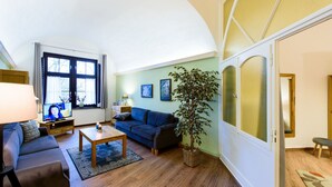 Un salon avec un canapé, une table basse et un téléviseur. Il y a une fenêtre avec des rideaux et une plante.