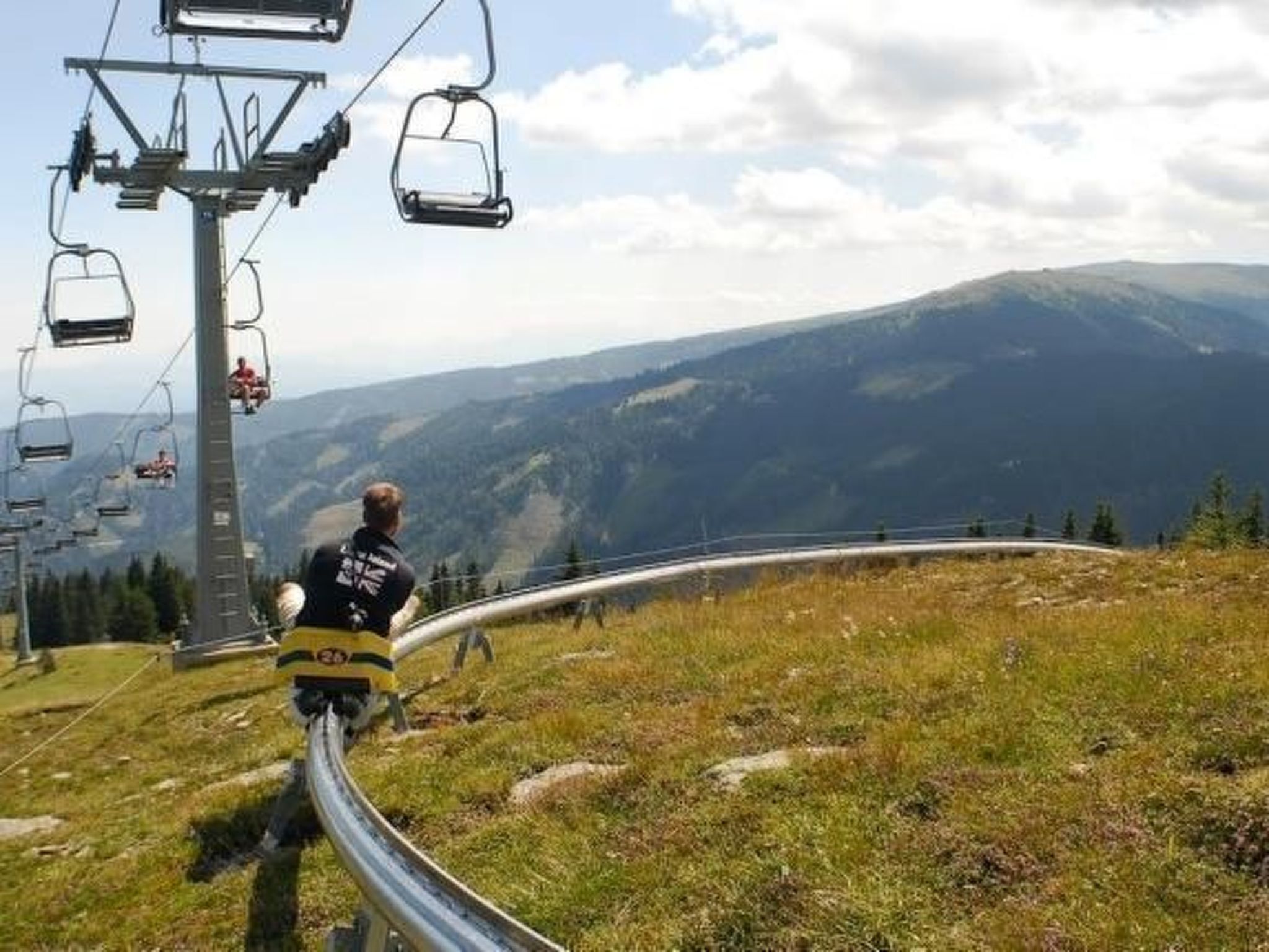 Eine Person fährt auf einem Mountainbike-Weg, im Hintergrund ist eine Seilbahn zu sehen.