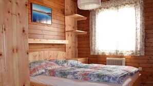 Een houten slaapkamer met een bed, een raam met gordijnen, een radiator en een schilderij aan de muur.