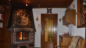 Een woonkamer met een schouw van baksteen, houten meubels en een deur met een decoratief glasraam.