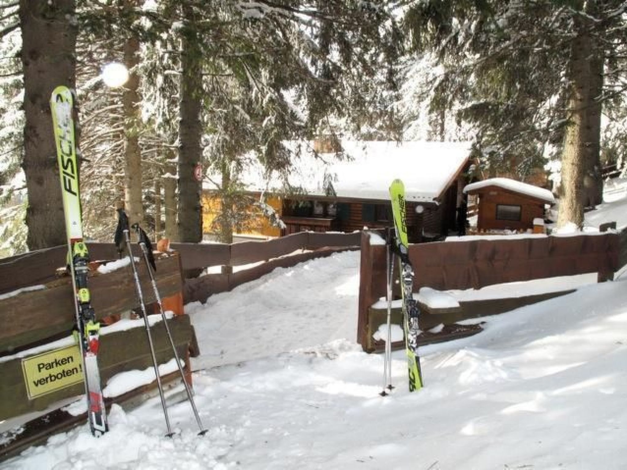 Een houten skigebied met ski’s en stokken, een houten omheining en een hutje op de achtergrond.