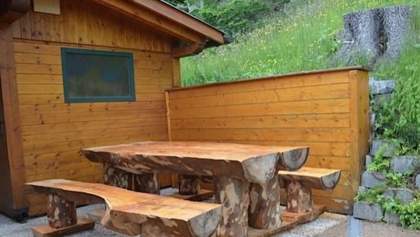 Een houten picknicktafel met bankjes, met op de achtergrond een houten blokhut.