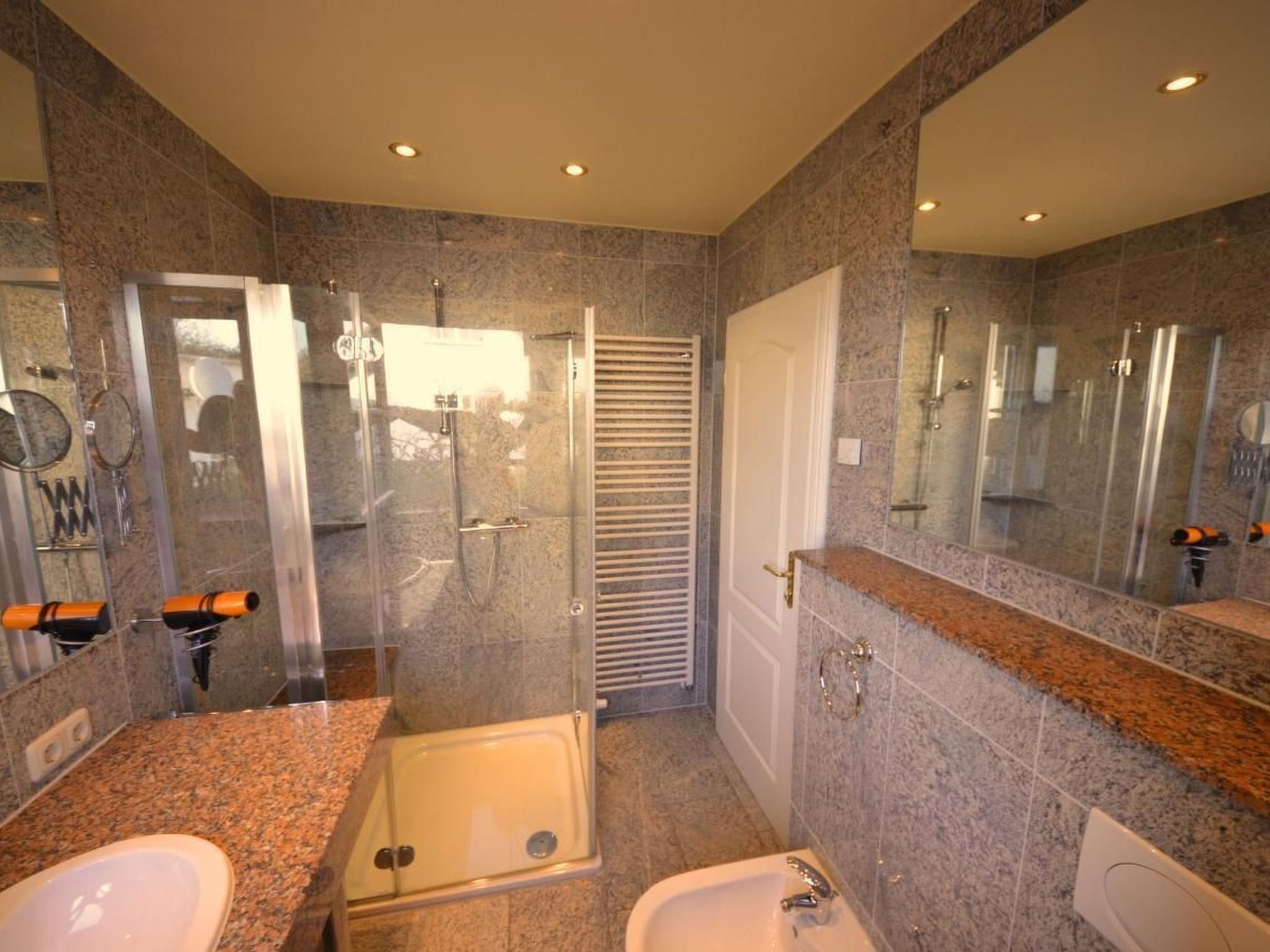 Un baño moderno con encimeras de granito, cabina de ducha con mampara de vidrio y un espejo grande.