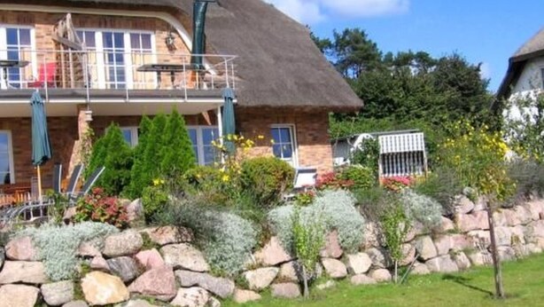 Een stenen huis met rieten dak, een balkon met buitenmeubilair, en een stenen muurtuin.