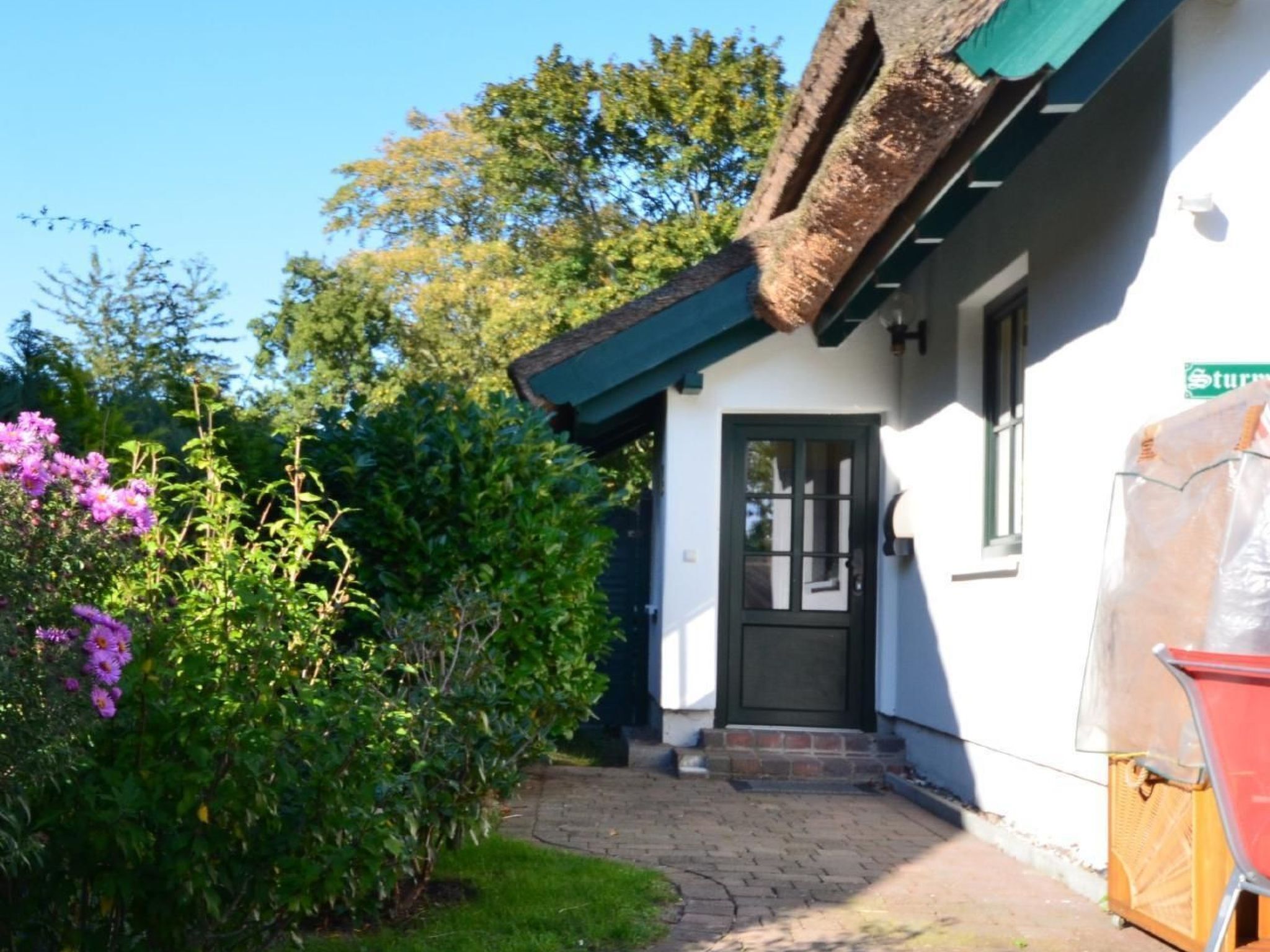Ein Haus mit einer schwarzen Tür, einem grünen Dach und einem Garten mit violetten Blumen.