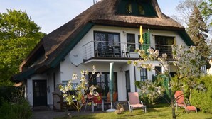 Ein traditionelles reetgedecktes Haus mit Balkon, umgeben von einem gepflegten Garten.