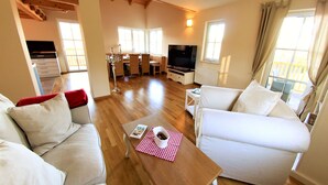 Een ruime woonkamer met een houten vloer, een witte bank, een tafel met een rood-wit geruit patroon en een televisie.