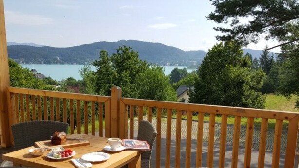 Een houten terras met tafel en stoelen, met uitzicht op een meer en bergen.