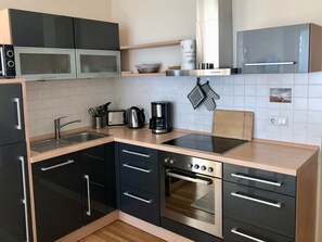 Eine moderne Küche mit schwarzen Schränken, einem Edelstahlbackofen, einer Mikrowelle und einer Kaffeemaschine.
