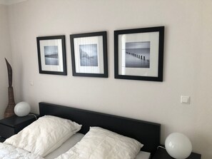 Un dormitorio con cabecera negra, ropa de cama blanca y tres fotografías enmarcadas en la pared.