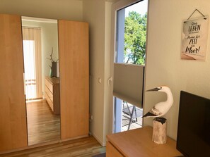 Ein Zimmer mit einer Schiebetür zu einem Flur, einem Fenster mit Jalousien, einem Holztisch mit einer weißen Vogel-Skulptur und einem an der Wand befestigten Schild mit Text.