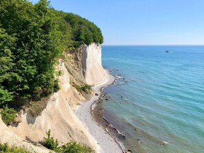 A coastal landscape with a sandy beach, a steep cliff, and a clear blue sea. - Traumappartement am Strand by Interhome (Breege)